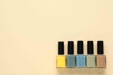 Photo of Bright nail polishes in bottles on beige background, flat lay. Space for text