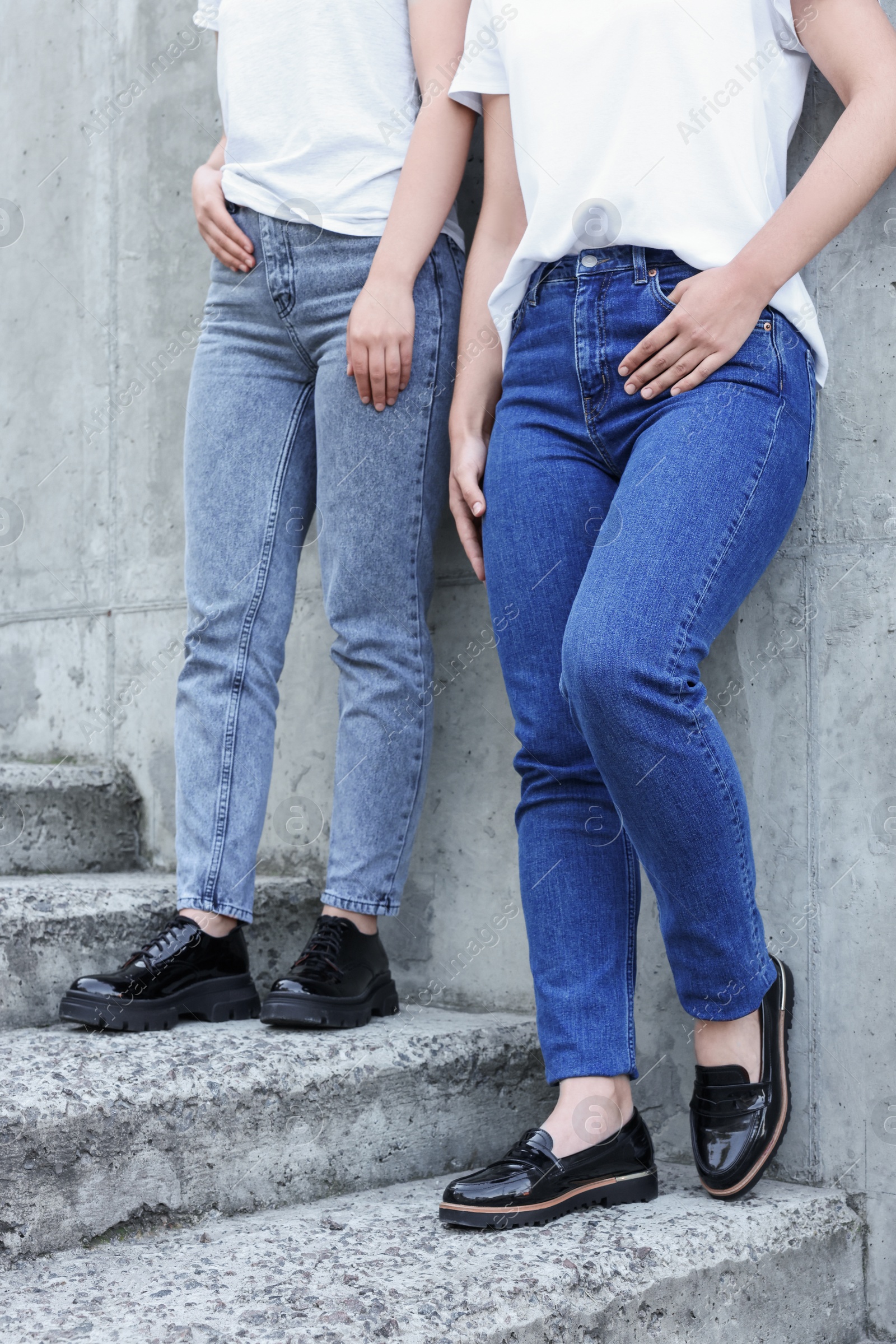 Photo of Women in stylish jeans on stairs near stone wall outdoors, closeup