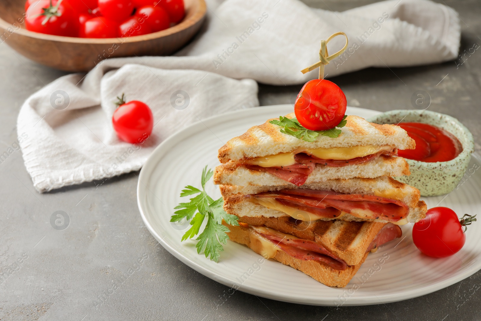 Photo of Stack of tasty sandwiches with ham and melted cheese served with tomato on grey textured table