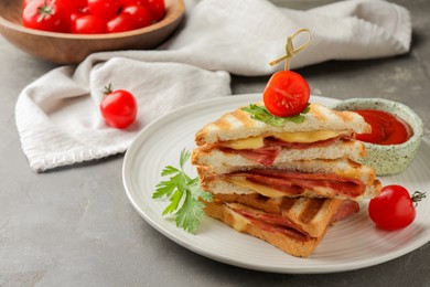 Stack of tasty sandwiches with ham and melted cheese served with tomato on grey textured table