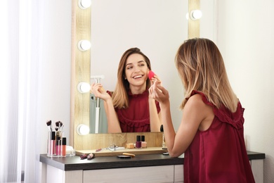 Photo of Woman applying makeup near mirror with light bulbs in dressing room