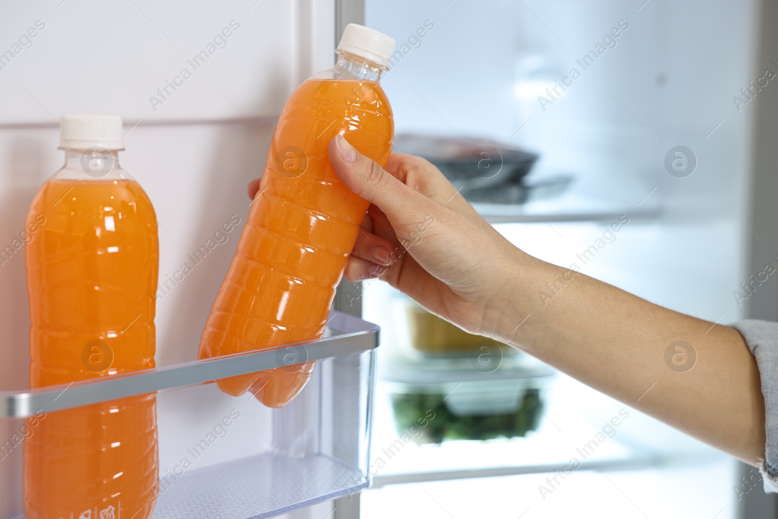 Photo of Young woman taking bottle of juice out of refrigerator, closeup