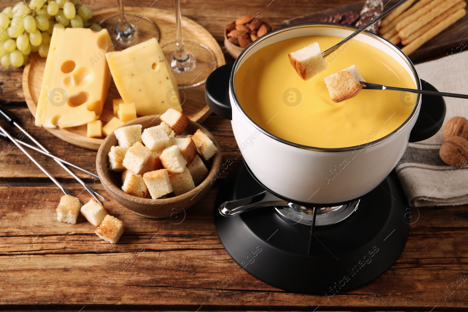 Photo of Dipping pieces of bread into tasty cheese fondue at wooden table