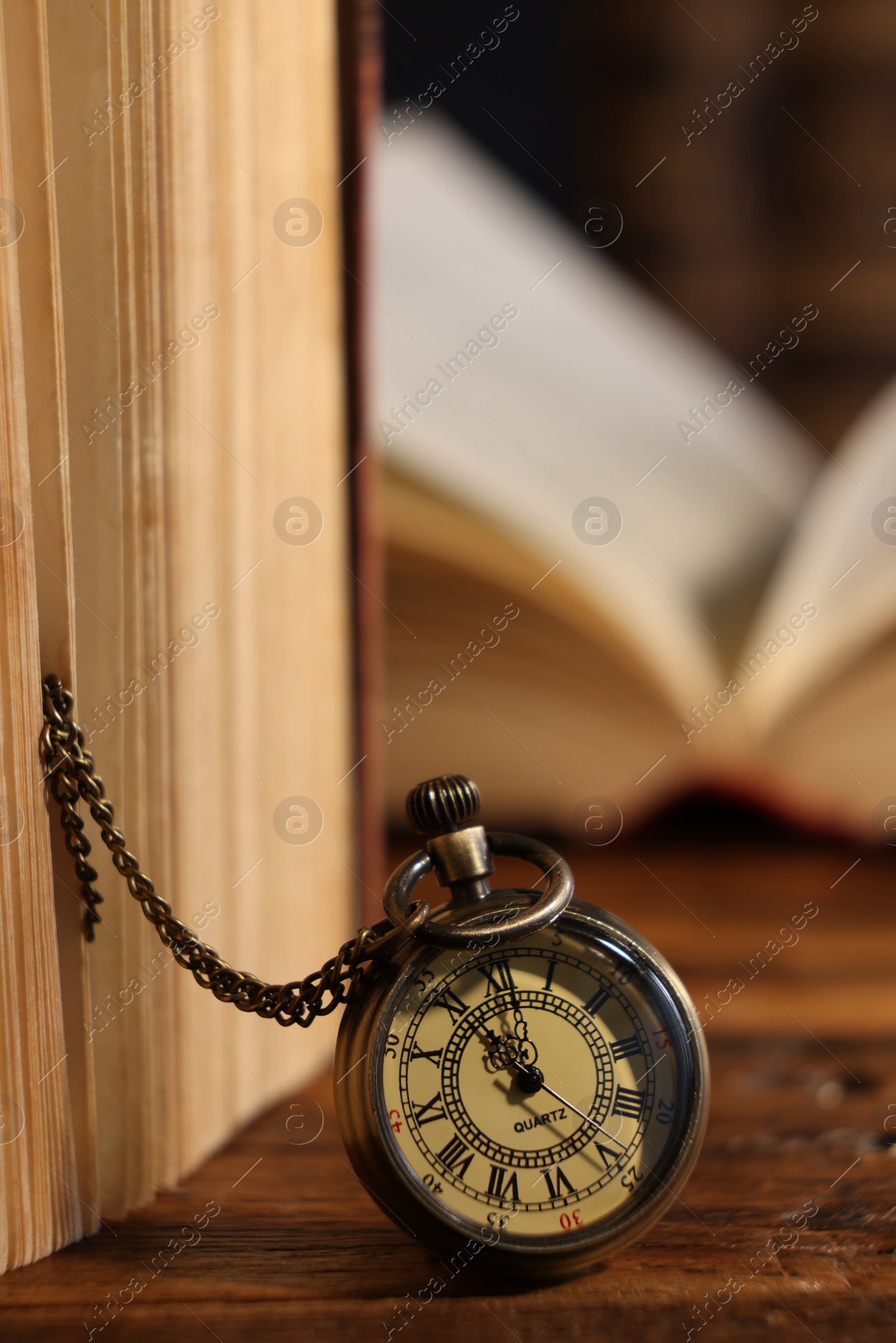 Photo of Pocket clock with chain and book on wooden table, closeup