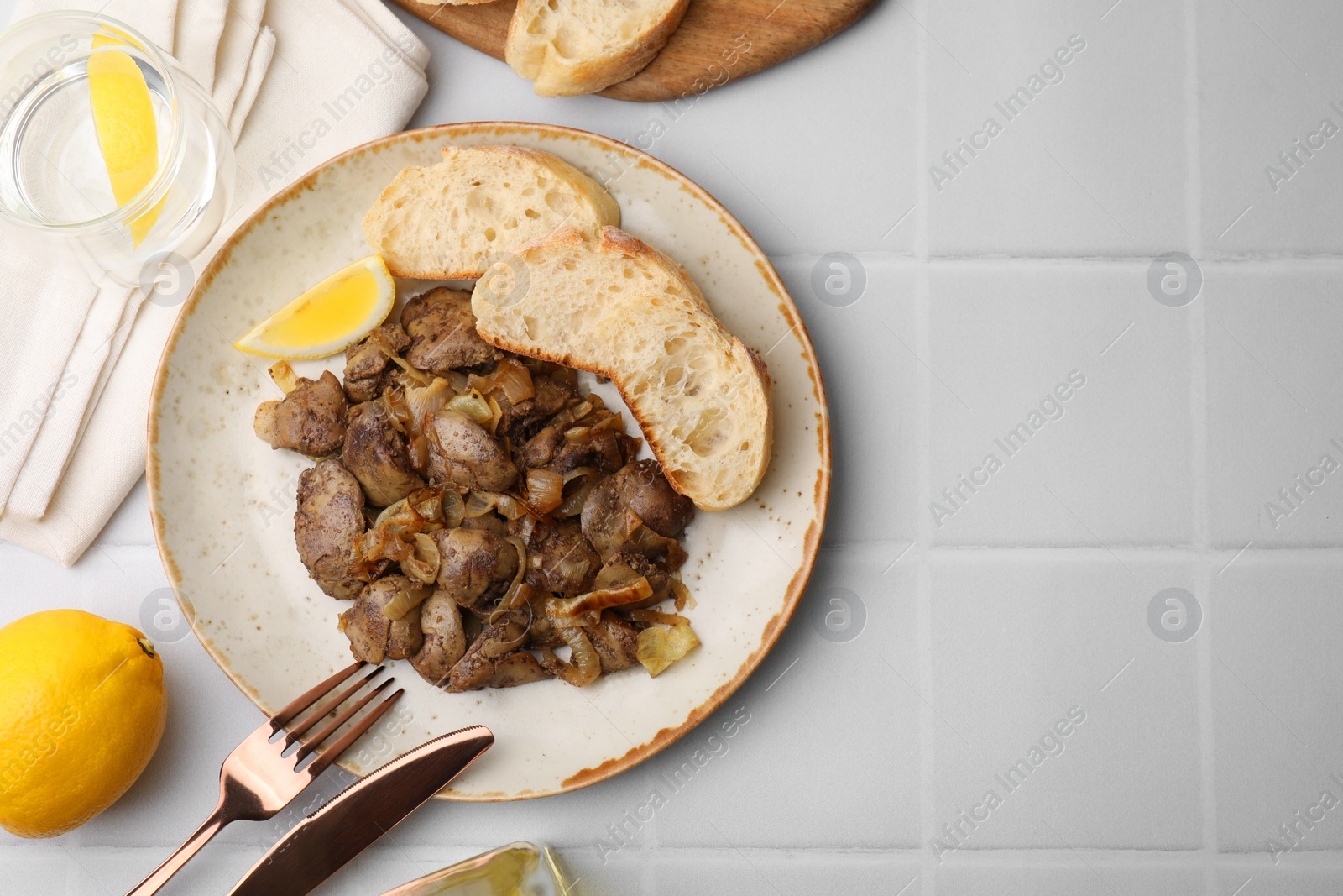 Photo of Tasty fried chicken liver with onion served on white tiled table, flat lay. Space for text