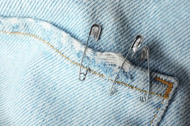 Metal safety pins on denim fabric, closeup