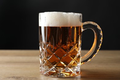 Mug with fresh beer on wooden table against black background, closeup