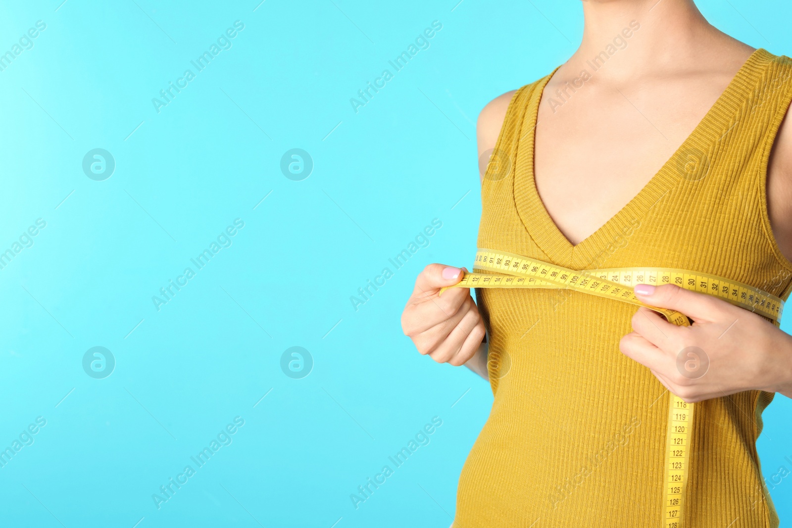 Photo of Young woman measuring breast size on color background, closeup view with space for text. Cosmetic surgery