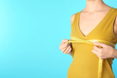 Photo of Young woman measuring breast size on color background, closeup view with space for text. Cosmetic surgery
