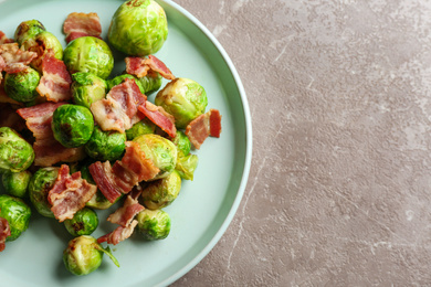 Photo of Delicious Brussels sprouts with bacon on marble table, above view. Space for text