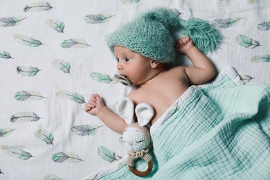Photo of Cute newborn baby in warm hat with pacifier and toy on bed, top view. Space for text