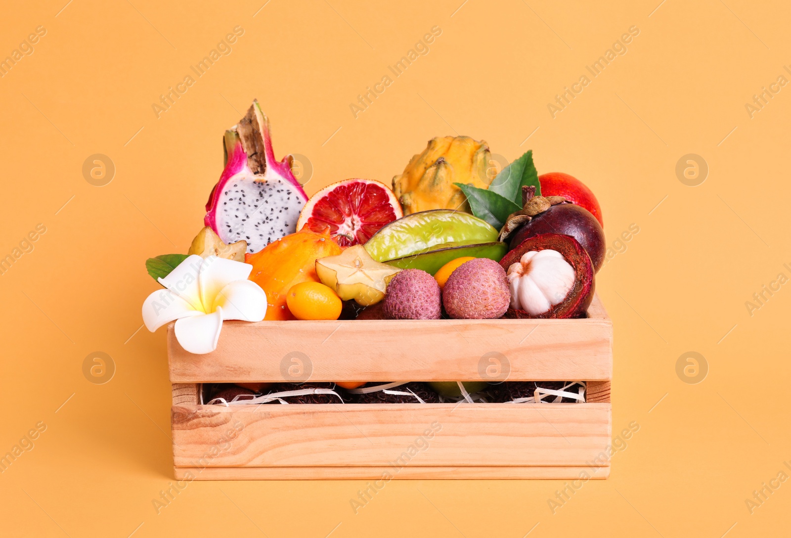 Photo of Different tropical fruits in wooden box on yellow background