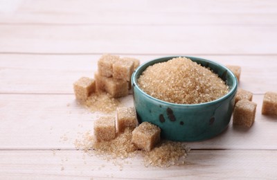 Photo of Refined and granulated brown sugar on white wooden table, closeup. Space for text