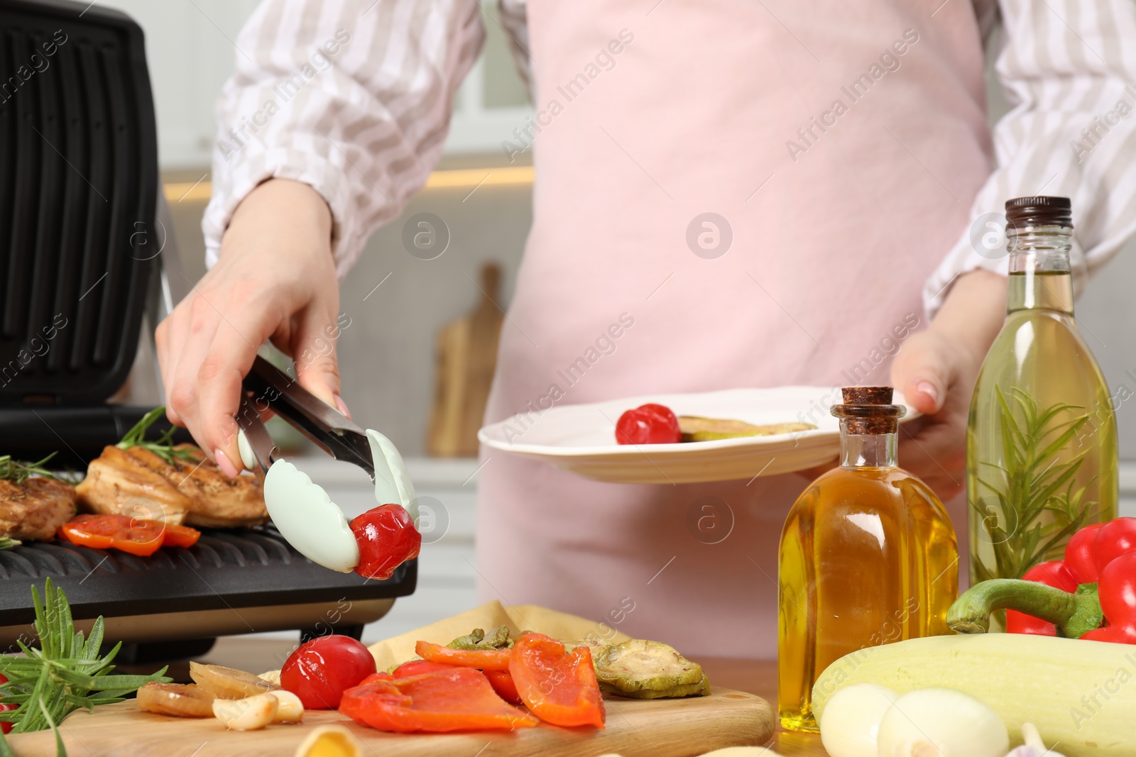 Photo of Woman cooking different products with electric grill at wooden table in kitchen, closeup