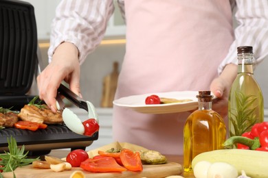 Photo of Woman cooking different products with electric grill at wooden table in kitchen, closeup