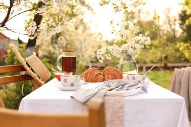 Photo of Stylish table setting with tea and croissants in spring garden