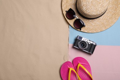 Beach towel, hat, sunglasses, camera and flip flops on sand, flat lay. Space for text