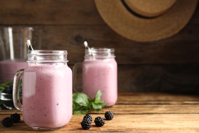 Photo of Tasty milk shake with blackberries on wooden table. Space for text