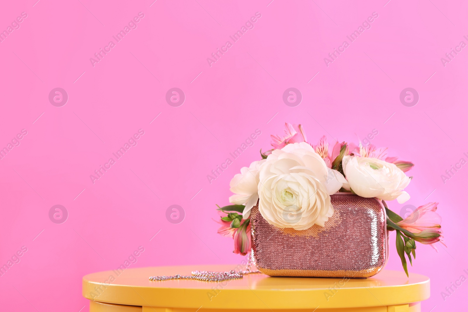 Photo of Elegant handbag with spring flowers on table against pink background, space for text