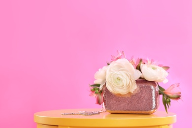 Photo of Elegant handbag with spring flowers on table against pink background, space for text