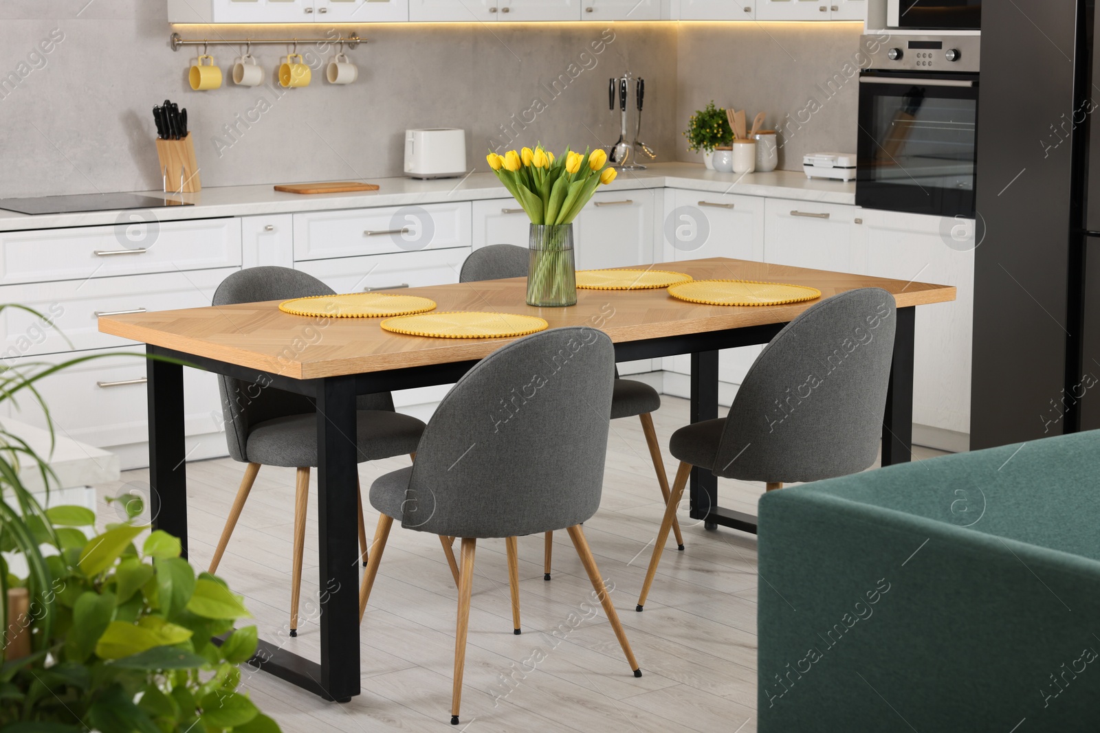 Photo of Spring atmosphere. Stylish kitchen interior with comfortable furniture and bouquet of beautiful yellow tulips