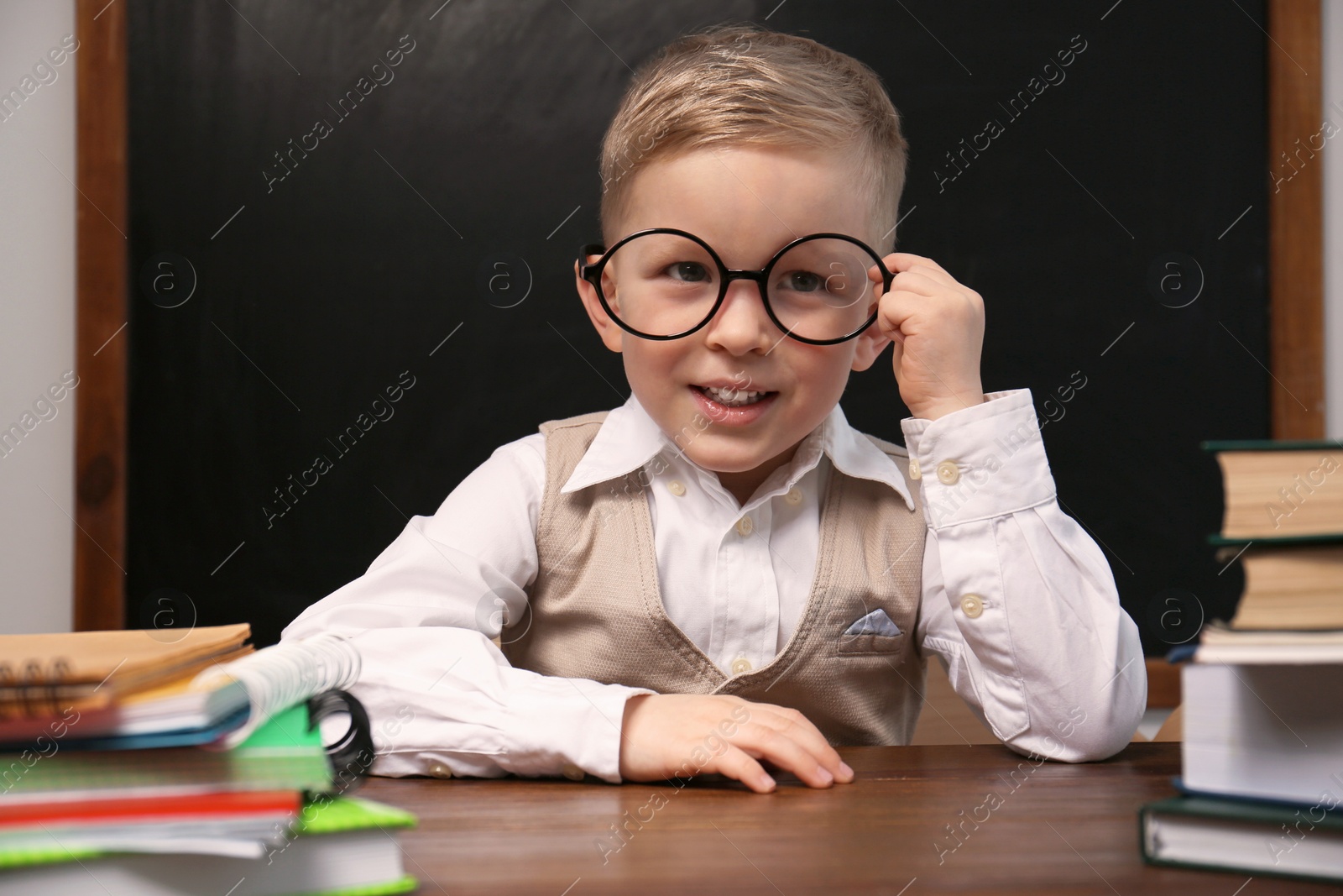 Photo of Cute little child wearing glasses at desk in classroom. First time at school