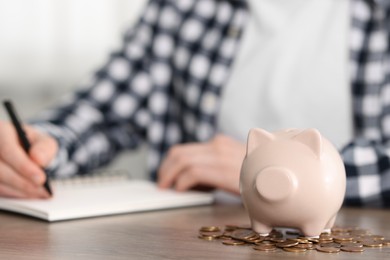 Financial savings. Man writing down notes at wooden table, focus on piggy bank and coins