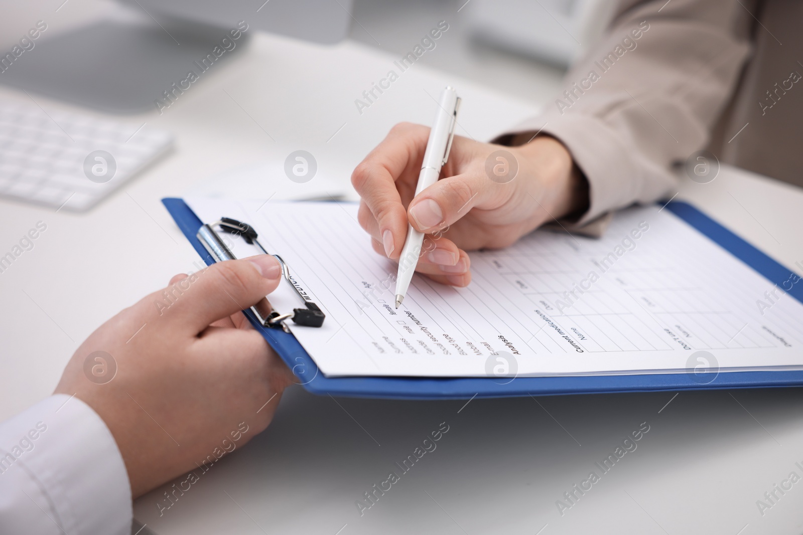 Photo of Doctor and patient filling medical card at white table, closeup