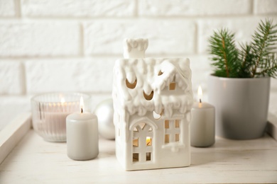 Photo of Composition with house shaped candle holder on white wooden table near brick wall. Christmas decoration
