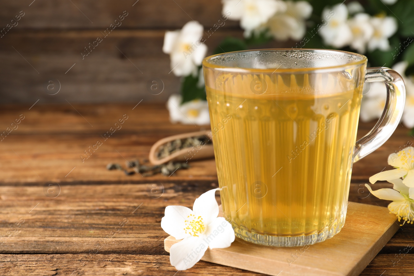 Photo of Cup of tea and fresh jasmine flowers on wooden table. Space for text