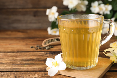 Photo of Cup of tea and fresh jasmine flowers on wooden table. Space for text