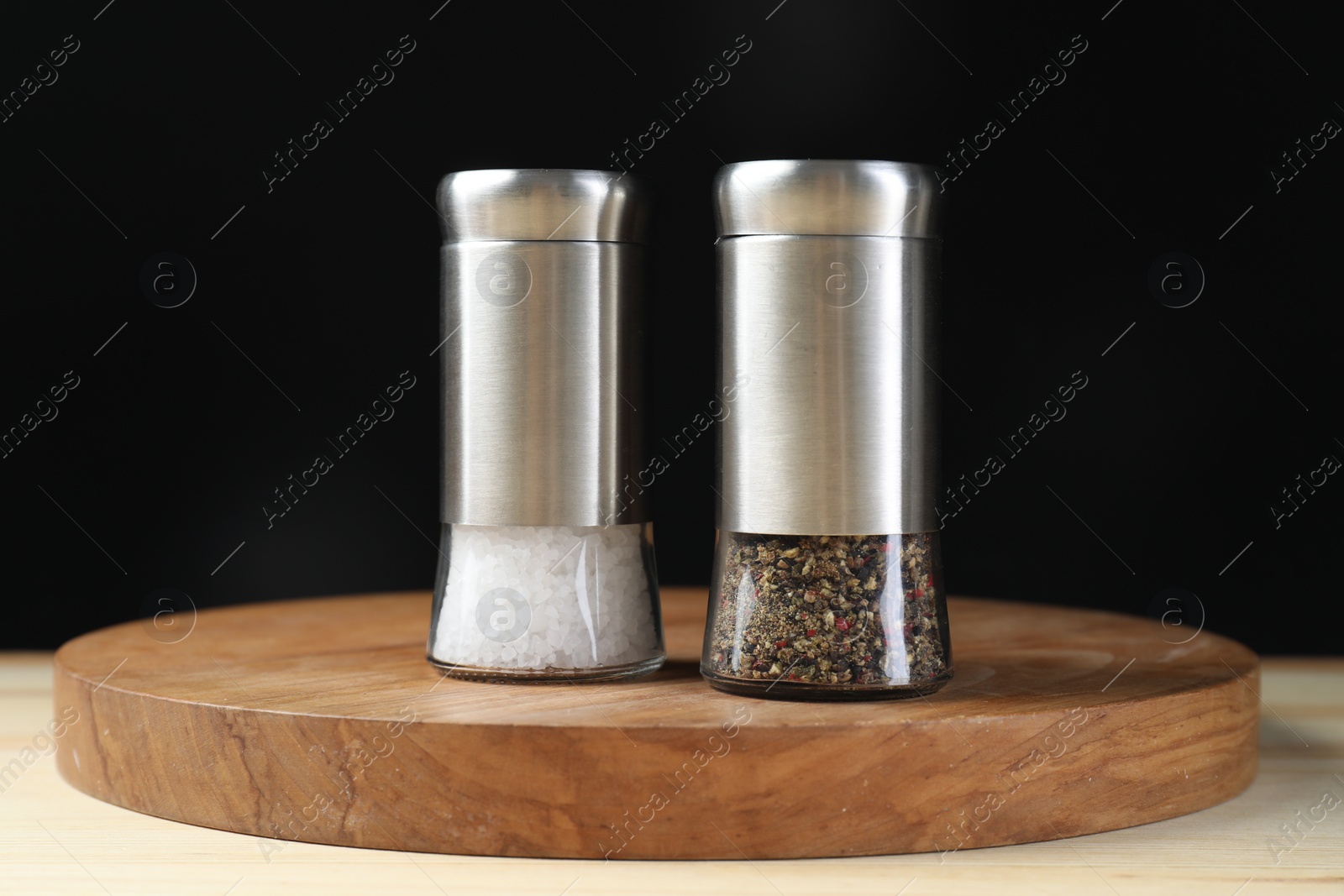 Photo of Salt and pepper shakers on wooden table against black background