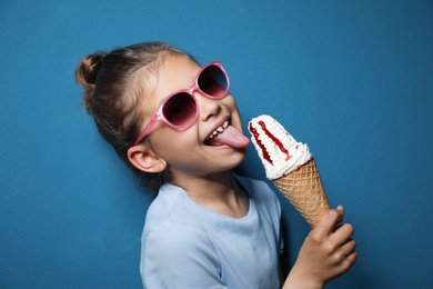 Adorable little girl with delicious ice cream against color background