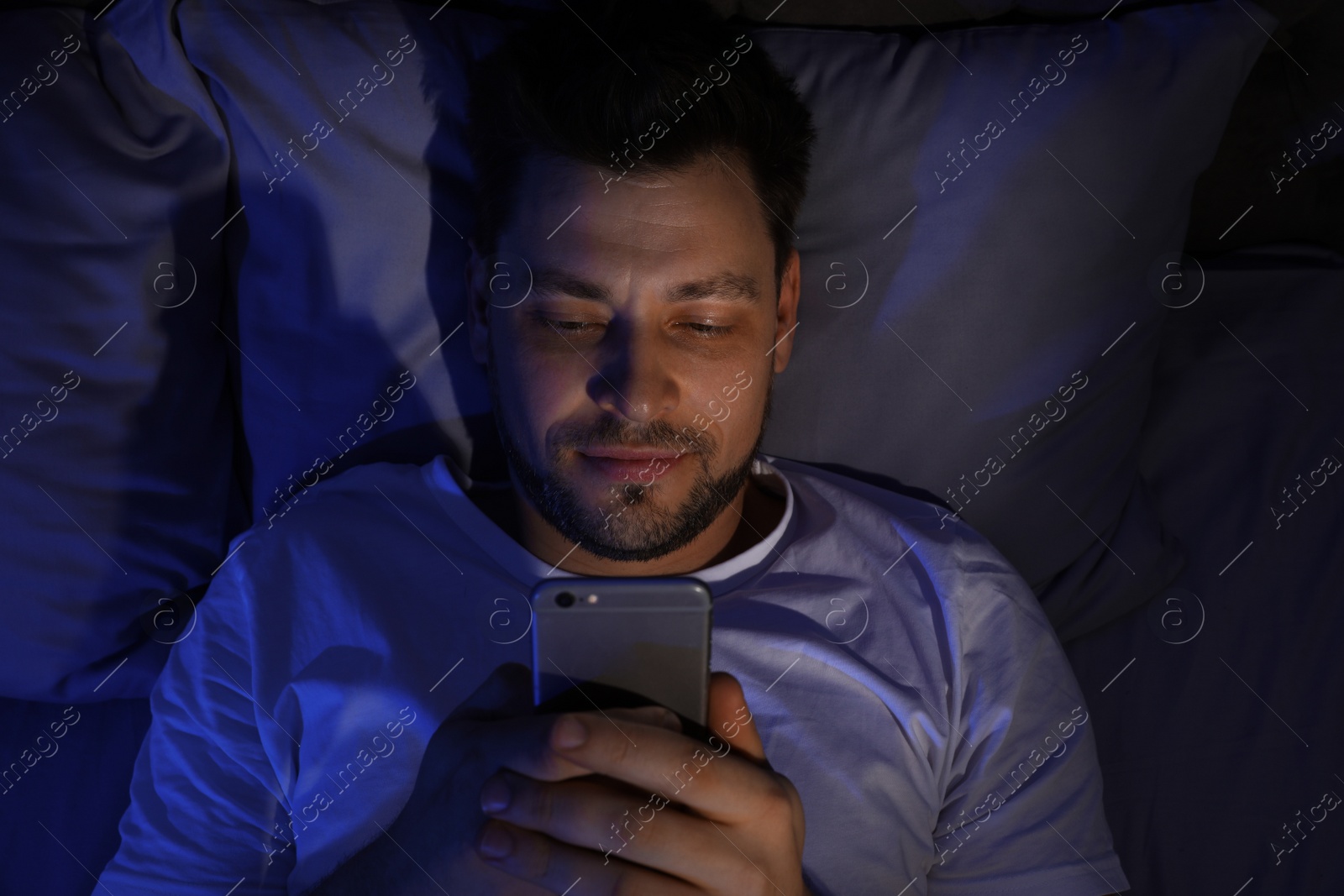 Photo of Handsome man using smartphone at night, view from above. Bedtime