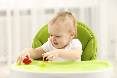Children toys. Cute little boy playing with spinning tops in high chair at home