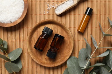 Aromatherapy products. Bottles of essential oil, sea salt and eucalyptus branches on bamboo mat, flat lay