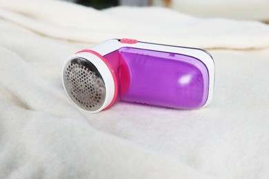 Photo of Modern fabric shaver on beige cloth indoors, closeup