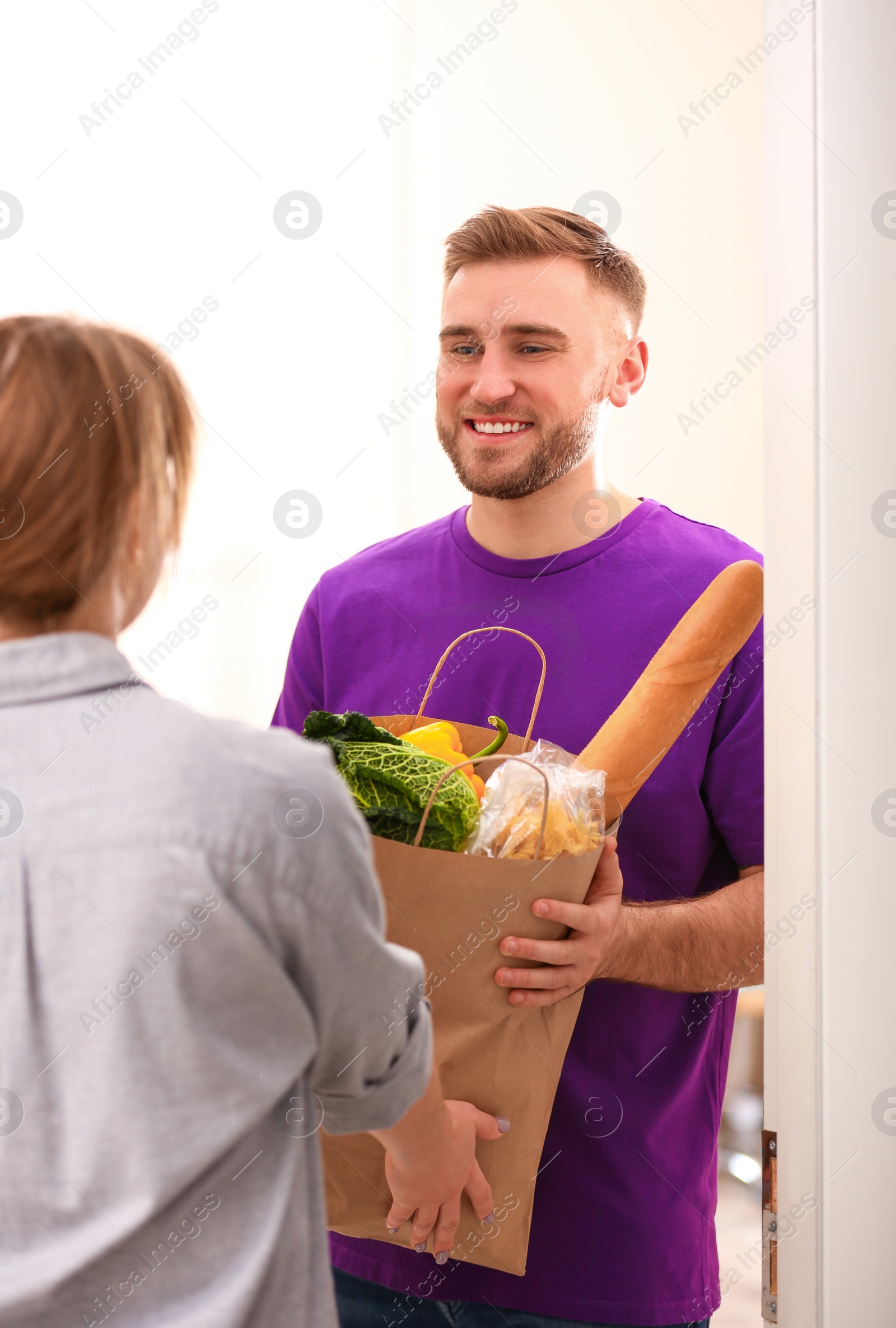 Photo of Courier giving paper bag with products to customer at home. Food delivery service