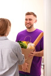 Photo of Courier giving paper bag with products to customer at home. Food delivery service