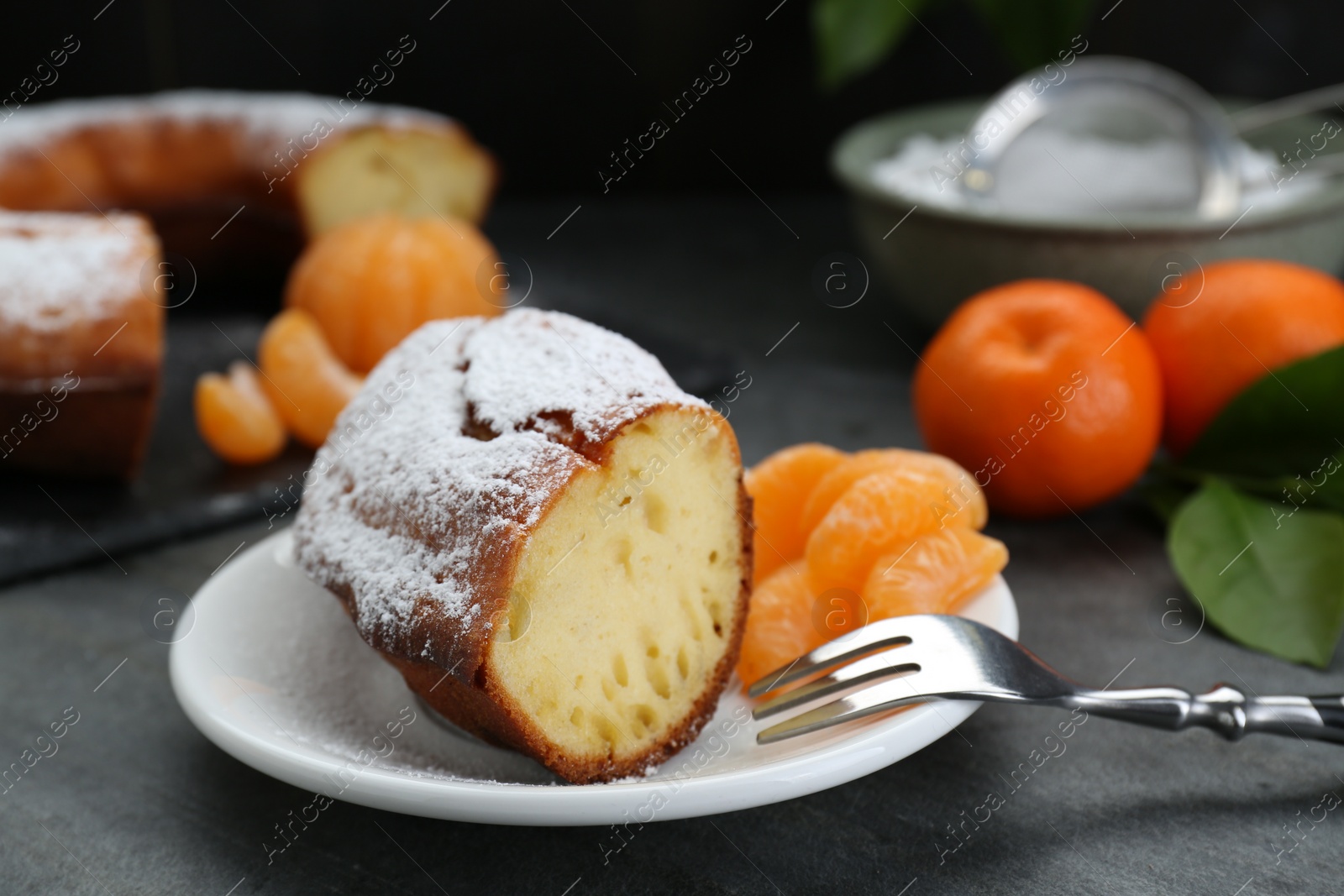 Photo of Piece of delicious homemade yogurt cake with powdered sugar and tangerines on gray table