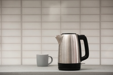 Photo of Modern electric kettle and cup on grey kitchen counter. Space for text