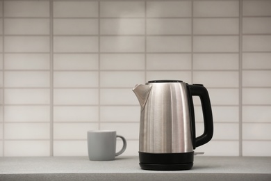 Modern electric kettle and cup on grey kitchen counter. Space for text