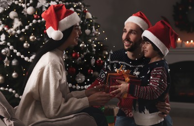 Image of Father with his cute son presenting gift to mother at home. Christmas celebration