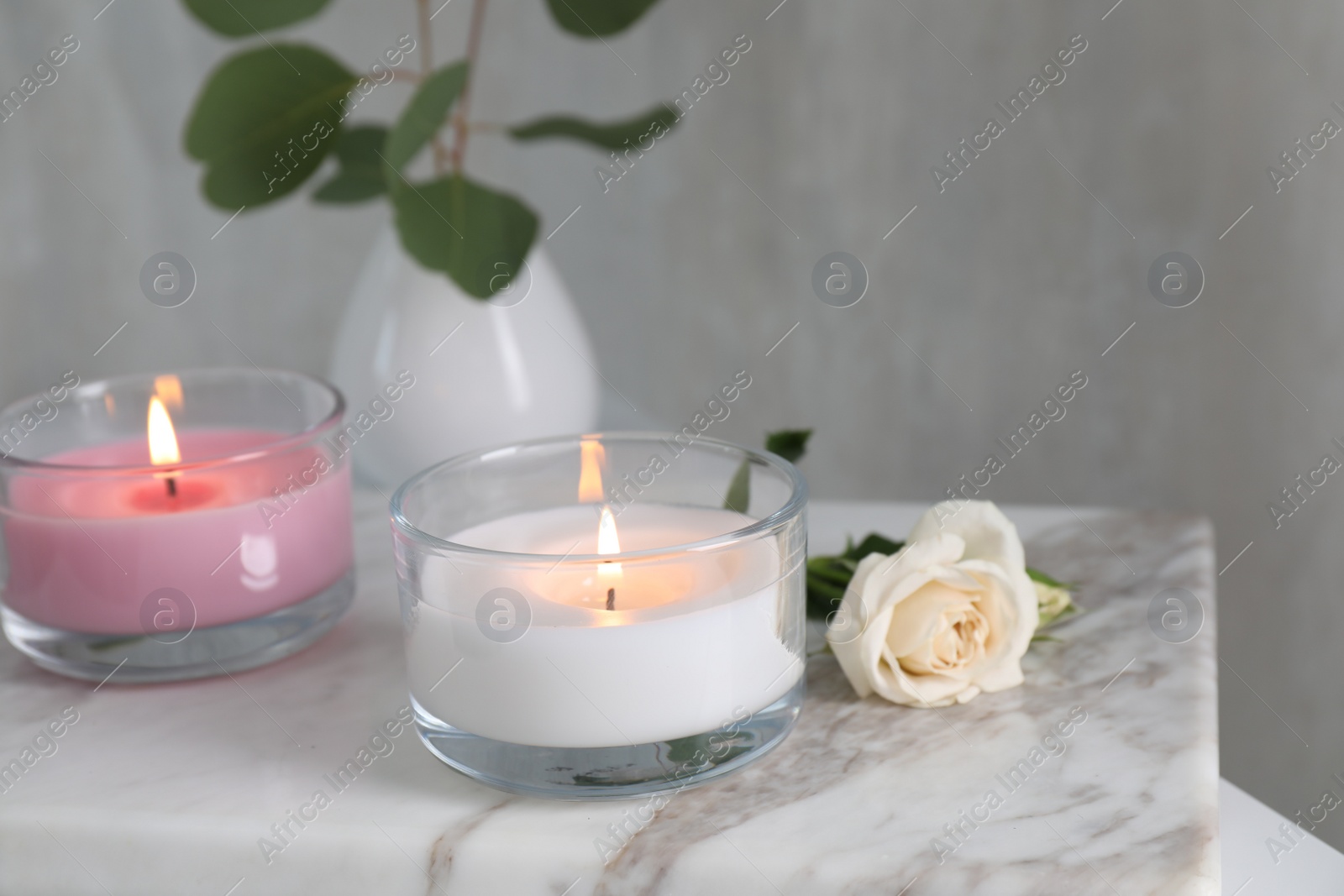 Photo of Burning candles and beautiful rose on white marble board