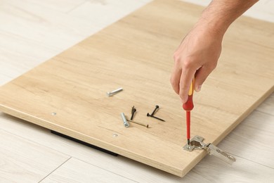 Man with screwdriver assembling furniture on floor, closeup