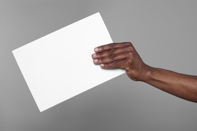 African American man holding sheet of paper on grey background, closeup. Mockup for design