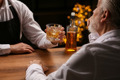 Bartender giving glass of whiskey to customer at bar counter, closeup
