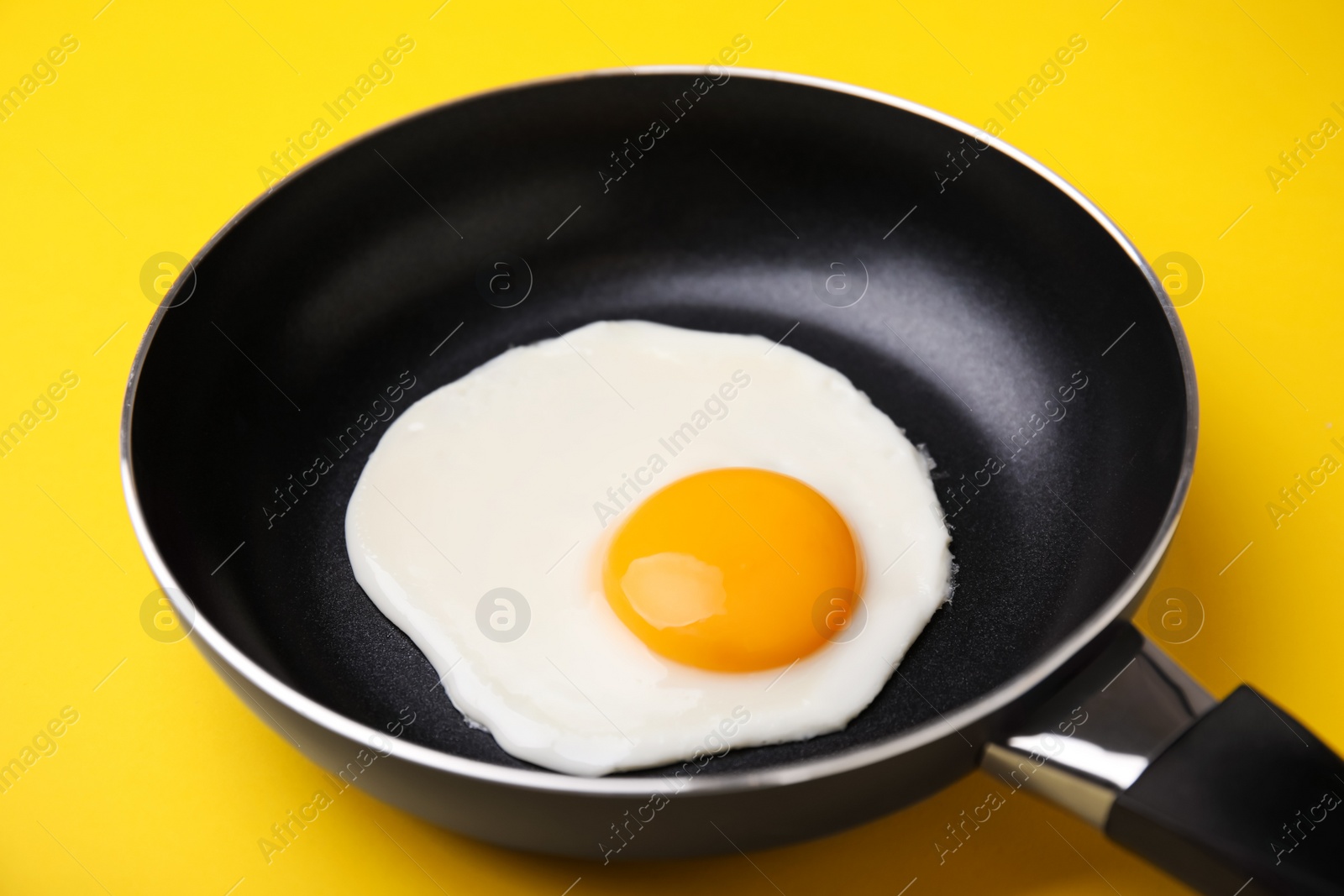 Photo of Tasty fried egg in pan on yellow background, closeup