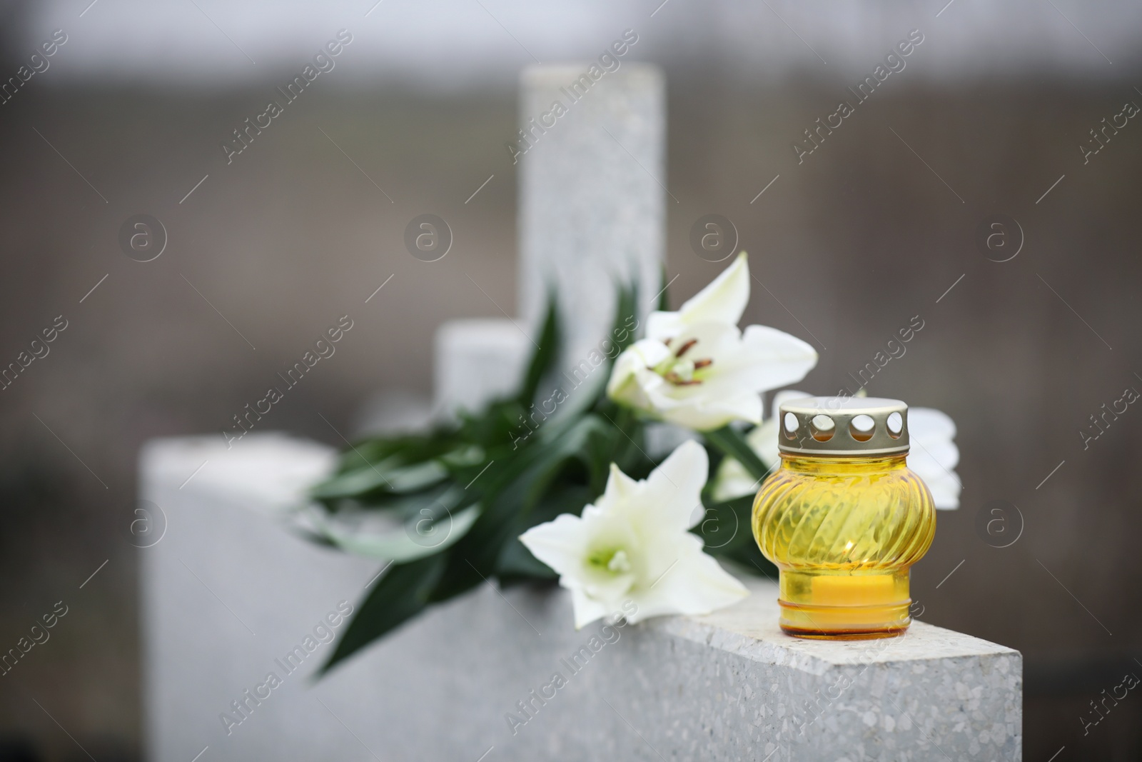 Photo of White lilies and candle on light grey granite tombstone outdoors. Funeral ceremony