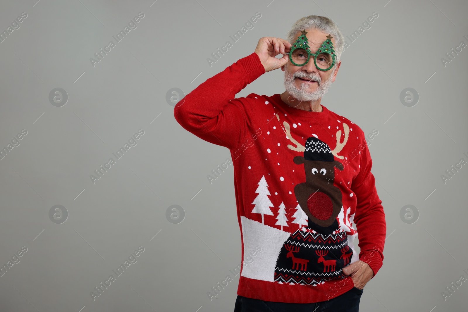 Photo of Senior man in Christmas sweater and funny glasses on grey background. Space for text